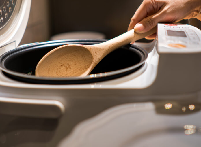 A Hand hold wooden ladle in electric rice cooker in the kitchen