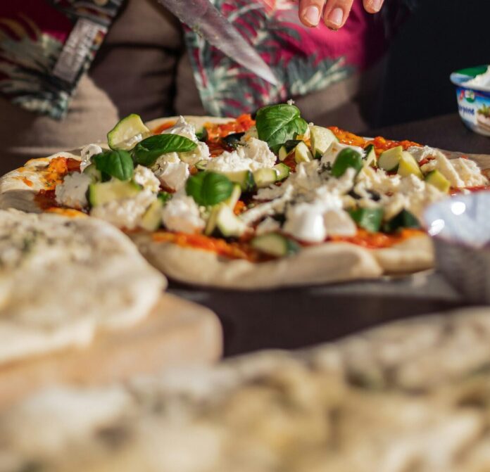 Hands placing toppings on a pizza