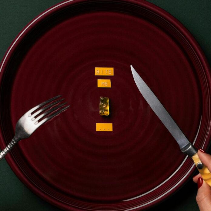 Person Holding A Fork and Knife With Gummy Bear and Sticker On Plate