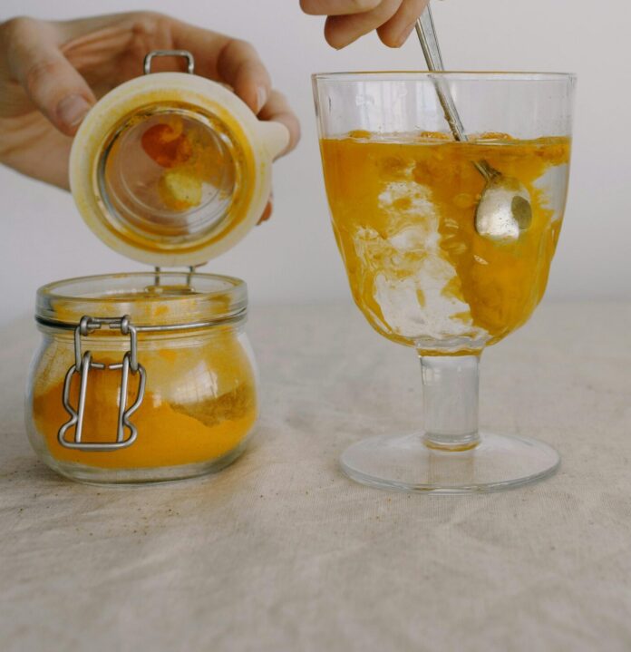 Crop hands adding turmeric in glass of hot water in morning