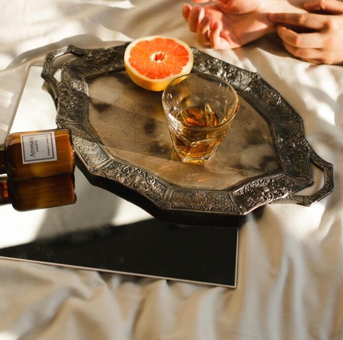 Crop woman on bed with cut orange and brandy indoors