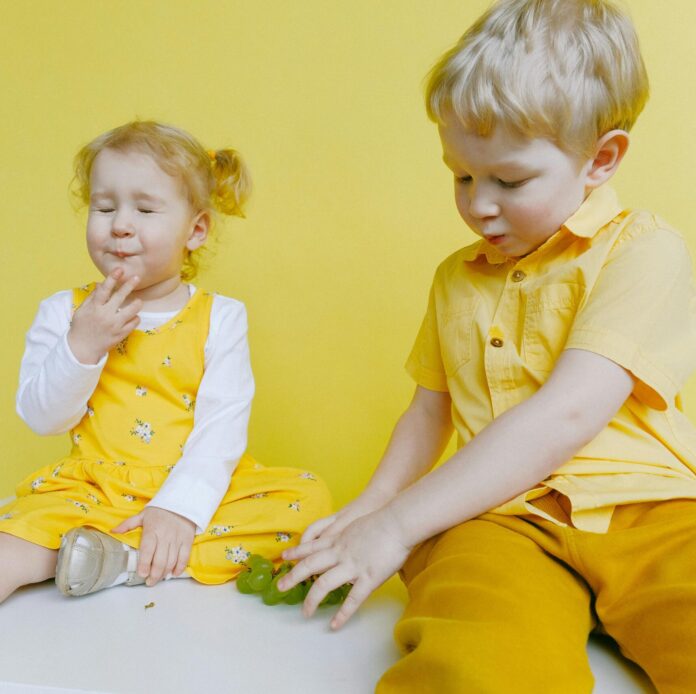 Toddlers Sitting On White Table While Eating Green Grapes